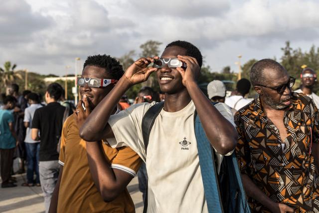 People watch through solar eclipse viewing glasses as the moon passes over the sun's horizon during a partial solar eclipse in Dakar on August 12, 2026. Throughout human history eclipses have stirred amazement, fear and reverence, as they appear to momentarily halt the normal course of nature, creating a strange twilight during which temperatures drop, shadows appear at strange angles and some animals go to sleep. (Photo by PATRICK MEINHARDT / AFP)