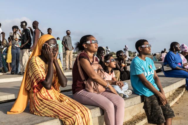 People watch through solar eclipse viewing glasses as the moon passes over the sun's horizon during a partial solar eclipse in Dakar on August 12, 2026. Throughout human history eclipses have stirred amazement, fear and reverence, as they appear to momentarily halt the normal course of nature, creating a strange twilight during which temperatures drop, shadows appear at strange angles and some animals go to sleep. (Photo by PATRICK MEINHARDT / AFP)