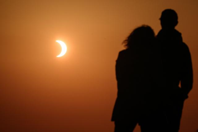 A couple watch the moon pass over the sun's horizon during a partial solar eclipse from the Chasseral peak, above Nods, northwestern Switzerland, on August 12, 2026. The eclipse was mainland Europe's first total eclipse since 2006. Throughout human history eclipses have stirred amazement, fear and reverence, as they appear to momentarily halt the normal course of nature, creating a strange twilight during which temperatures drop, shadows appear at strange angles and some animals go to sleep. (Photo by Fabrice COFFRINI / AFP)