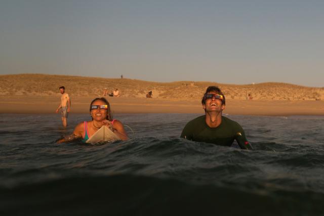 surfers watch a partial solar eclipse in the water in Lege-Cap-Ferret on August 12, 2026. Millions of people turn their gaze towards the heavens on August 12, 2026 to witness one of nature's greatest spectacles -- a rare total solar eclipse -- as it sweeps over mainland Europe to briefly turn day into night. (Photo by Tania Buijten / AFP)