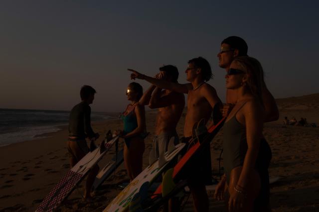 surfers watch a partial solar eclipse in the water in Lege-Cap-Ferret on August 12, 2026. Millions of people turn their gaze towards the heavens on August 12, 2026 to witness one of nature's greatest spectacles -- a rare total solar eclipse -- as it sweeps over mainland Europe to briefly turn day into night. (Photo by Tania Buijten / AFP)