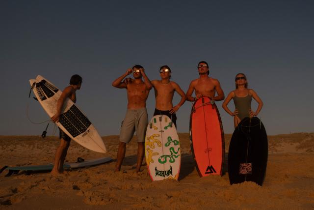 surfers watch a partial solar eclipse in the water in Lege-Cap-Ferret on August 12, 2026. Millions of people turn their gaze towards the heavens on August 12, 2026 to witness one of nature's greatest spectacles -- a rare total solar eclipse -- as it sweeps over mainland Europe to briefly turn day into night. (Photo by Tania Buijten / AFP)