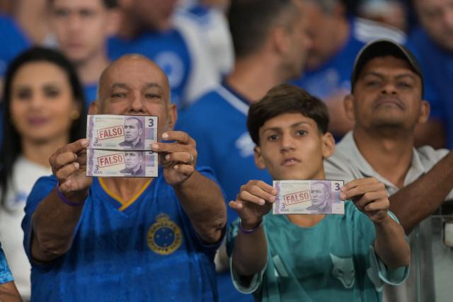 Cruzeiro supporters hold mock banknotes reading "FALSE" and bearing the image of Flamengo Portuguese head coach Leonardo Jardim, a former Cruzeiro coach, ahead of the first leg of the Copa Libertadores round of 16 football match between Brazilian teams Cruzeiro and Flamengo at the Mineirao stadium in Belo Horizonte, Minas Gerais state, Brazil, on August 12, 2026. (Photo by DOUGLAS MAGNO / AFP)