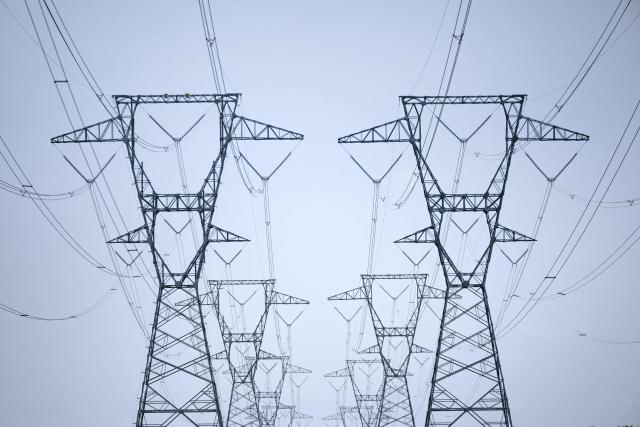 Transmission towers and power lines are shown adjacent to single-family homes with nearby data center infrastructure in Stone Ridge, Virginia on August 12, 2026. Hastily built to meet skyrocketing demand for computing power required by the global artificial intelligence race, data centers are facing opposition across the United States. (Photo by Brendan Smialowski / AFP)