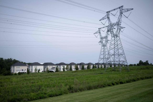 Transmission towers and power lines are shown adjacent to single-family homes with nearby data center infrastructure in Stone Ridge, Virginia on August 12, 2026. Hastily built to meet skyrocketing demand for computing power required by the global artificial intelligence race, data centers are facing opposition across the United States. (Photo by Brendan Smialowski / AFP)