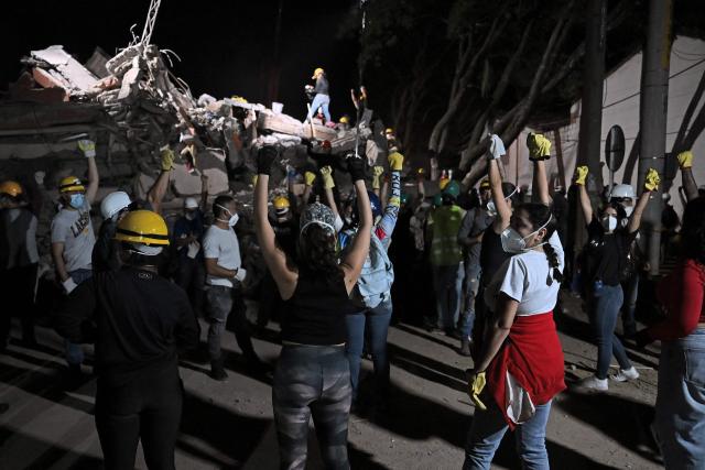 Rescue workers ask for silence with their fist up as they search for survivors at the site of collapsed buildings after an earthquake in Cali, Colombia on August 12, 2026. Rescuers, soldiers and volunteers searched through collapsed apartment blocks and office buildings across western Colombia, racing to find survivors after the country's strongest earthquake in a century killed at least 239 people and left many more homeless on August 10, 2026. The 7.4-magnitude quake injured more than 1,670 people, according to a tally by municipal authorities. (Photo by Raul ARBOLEDA / AFP)