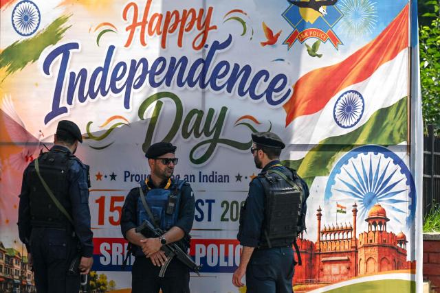 Security personnel stand guard near a poster wishing Independence Day ahead of its celebrations in Srinagar on August 13, 2026. (Photo by Tauseef MUSTAFA / AFP)
