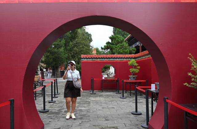 A foreign tourist records with her mobile phone as people visit the Jingshan park in Beijing on August 13, 2026. (Photo by Adek BERRY / AFP)
