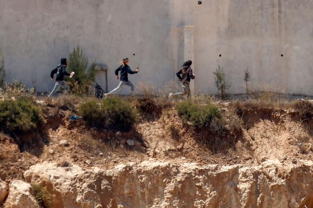 Israeli settlers run as being chased by an Israeli military vehicle around Palestinian houses in the village of Qusra, south of Nablus, in the occupied West Bank, on August 13, 2026. Israel has occupied the West Bank since 1967. More than 500,000 Israelis live in settlements in the territory, which are illegal under international law, among some three million Palestinians. Violence against Palestinians by Israeli settlers has increased dramatically since the October 7, 2023 attack on Israel by Hamas from the Gaza Strip. (Photo by Zain JAAFAR / AFP)