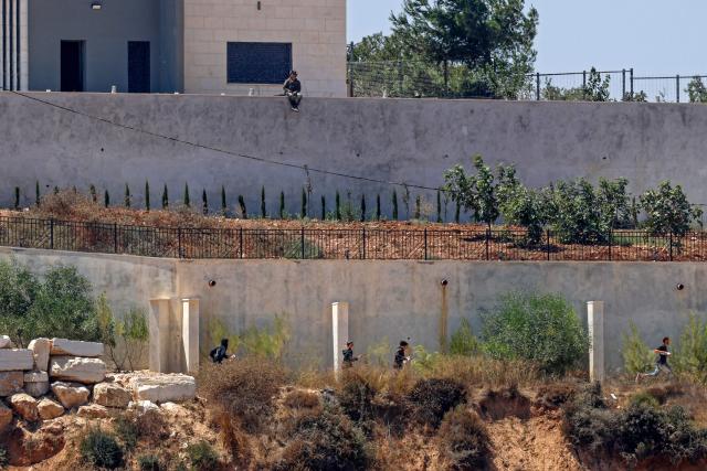 Israeli settlers run as being chased by an Israeli military vehicle, while a soldier sits on the boundary wall of a Palestinian house in the village of Qusra, south of Nablus, in the occupied West Bank, on August 13, 2026. Israel has occupied the West Bank since 1967. More than 500,000 Israelis live in settlements in the territory, which are illegal under international law, among some three million Palestinians. Violence against Palestinians by Israeli settlers has increased dramatically since the October 7, 2023 attack on Israel by Hamas from the Gaza Strip. (Photo by Zain JAAFAR / AFP)