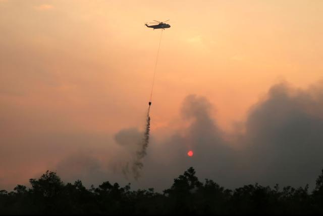 A helicopter drops water on burning forests and land in the Petuk Katimpun area, Palangka Raya, in Indonesia's Central Kalimantan province, on August 13, 2026. (Photo by REINA / AFP)