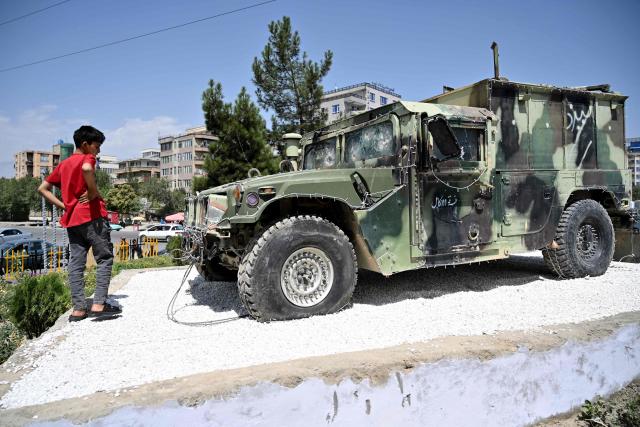 An Afghan boy looks at a damaged armored Humvee displayed at a square in Kabul on August 13, 2026 ahead of the fifth anniversary marking the Taliban's return to power. (Photo by Wakil KOHSAR / AFP)