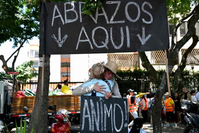 People hug each other at a hugging booth as they hold a sign that reads in Spanish "Cheer Up" three days after a 7.4 earthquake in Cali, Colombia, on August 13, 2026, Rescuers in Colombia were making last-ditch efforts to locate earthquake survivors early on August 13, 2026, as the critical 72-hour window for rescue operations neared its end. (Photo by Raul ARBOLEDA / AFP)