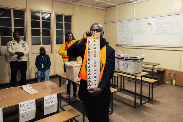 TOPSHOT - Voting station presiding officer holds a marked ballot during the counting process at Woodlands Primary School in Lusaka on August 13, 2026. Zambians flocked to the polls on August 13 for a vote focused on economic hardships in the copper-rich nation, where President Hakainde Hichilema is seeking a second term. Most polling stations closed as scheduled at 6:00 pm (1600 GMT), with counting expected to begin the same night and results in the presidential vote due by August 17. (Photo by GIANLUIGI GUERCIA / AFP)