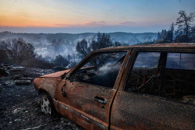 This photograph shows a burnt car after a wildfire near the village of Siviri, northern Greece, on August 13, 2026. A fleet of small boats evacuated hundreds of tourists from beaches in northern Greece as a forest fire bore down on two popular resorts. Water bombing planes and helicopters and almost 150 firefighters battled the flames spreading across the Halkidiki peninsula, south of the city of Thessaloniki, the fire service said. (Photo by Vasilis VERVERIDIS / AFP)