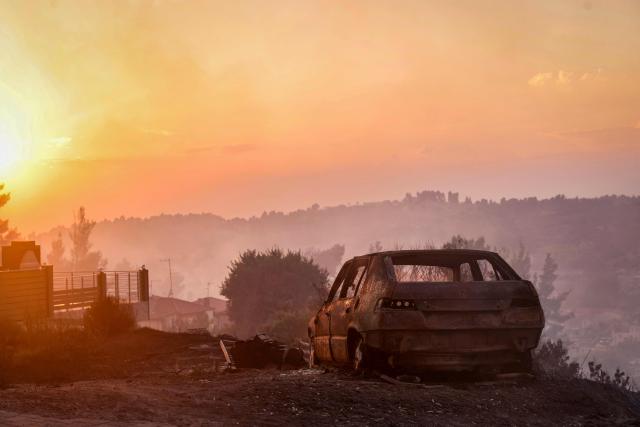This photograph shows a burnt car after a wildfire near the village of Siviri, northern Greece, on August 13, 2026. A fleet of small boats evacuated hundreds of tourists from beaches in northern Greece as a forest fire bore down on two popular resorts. Water bombing planes and helicopters and almost 150 firefighters battled the flames spreading across the Halkidiki peninsula, south of the city of Thessaloniki, the fire service said. (Photo by Vasilis VERVERIDIS / AFP)