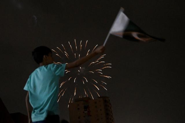 A boy waves a flag as he watches a firework explode during celebrations ahead of Pakistan's 79th anniversary of Independence Day in Karachi on August 14, 2026. (Photo by Rizwan TABASSUM / AFP)