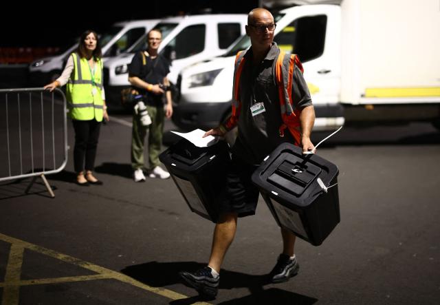 Ballot boxes are carried into the count centre venue for the by-election of the parliamentary seat of Clacton, at Clacton Leisure Centre, eastern England on August 13, 2026. Voters in eastern England headed to the polls on August 13 for a by-election triggered by hard-right Reform UK leader Nigel Farage. (Photo by Henry Nicholls / AFP)