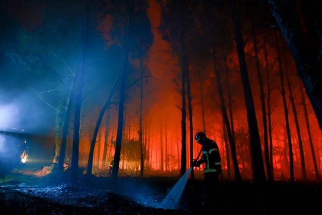 A firefighter hoses down the charred ground as flames continue to burn in the Landes forest in Luglon, southwestern France, in the early hours of August 14, 2026. The fire that broke out on August 13, 2026 in the Landes forest has now spread across 400 hectares, and 400 people "are being evacuated as a precautionary measure", according to the prefecture of this south-western department. (Photo by ROMAIN PERROCHEAU / AFP)