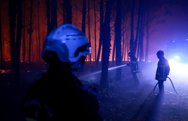 A firefighter hoses down the charred ground as flames continue to burn in the Landes forest in Luglon, southwestern France, in the early hours of August 14, 2026. The fire that broke out on August 13, 2026 in the Landes forest has now spread across 400 hectares, and 400 people "are being evacuated as a precautionary measure", according to the prefecture of this south-western department. (Photo by ROMAIN PERROCHEAU / AFP)