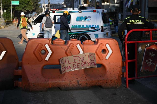 A police officer stands next to a sign reading "Silence, rescue zone" in Cali, Colombia, on August 13, 2026, three days after a 7.4-magnitude earthquake struck the region. Rescuers in Colombia were making last-ditch efforts to locate earthquake survivors early on August 13, 2026, as the critical 72-hour window for rescue operations neared its end. (Photo by Raul ARBOLEDA / AFP)