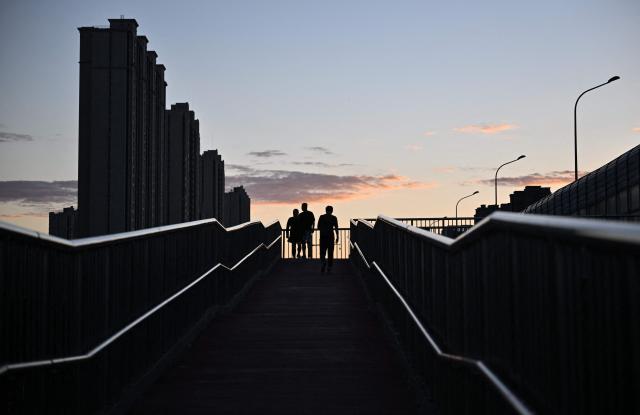 People walk on a bridge at dusk in Beijing on August 13, 2026. (Photo by ADEK BERRY / AFP)