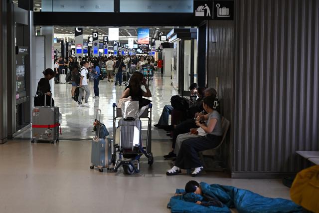 People line up in front of the check-in counter as a passenger (R) sleeping on the floor at the Narita International Airport in Narita, Chiba prefecture on August 14, 2026. (Photo by Andrew CABALLERO-REYNOLDS / AFP)
