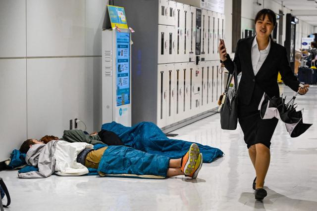 People sleep on the floor of the terminal 2 of Narita International Airport in Narita, Chiba prefecture on August 14, 2026. (Photo by Andrew CABALLERO-REYNOLDS / AFP)