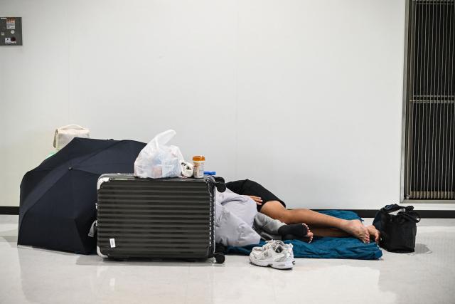 People sleep on the floor of the terminal 2 of Narita International Airport in Narita, Chiba prefecture on August 14, 2026. (Photo by Andrew CABALLERO-REYNOLDS / AFP)