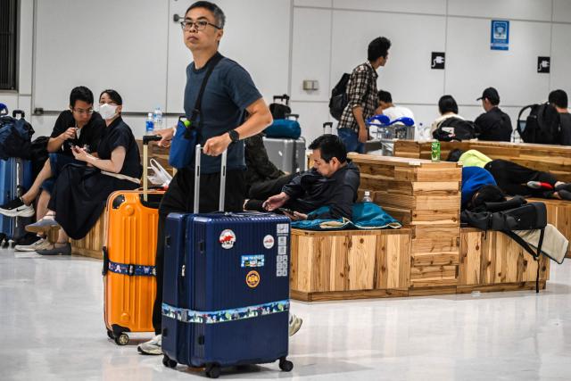 A passenger (L) walks with his suitcases at the Narita International Airport in Narita, Chiba prefecture on August 14, 2026. At least four people died in eastern Japan after "unprecedented" heavy rain that left thousands stranded at Narita airport overnight and snarled up roads and rail services, authorities said. (Photo by Andrew CABALLERO-REYNOLDS / AFP)