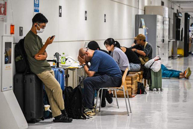 People rest at the Narita International Airport in Narita, Chiba prefecture on August 14, 2026. At least four people died in eastern Japan after "unprecedented" heavy rain that left thousands stranded at Narita airport overnight and snarled up roads and rail services, authorities said. (Photo by Andrew CABALLERO-REYNOLDS / AFP)