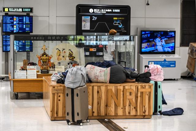 People sleep at the terminal 2 of Narita International Airport in Narita, Chiba prefecture on August 14, 2026. At least four people died in eastern Japan after "unprecedented" heavy rain that left thousands stranded at Narita airport overnight and snarled up roads and rail services, authorities said. (Photo by Andrew CABALLERO-REYNOLDS / AFP)