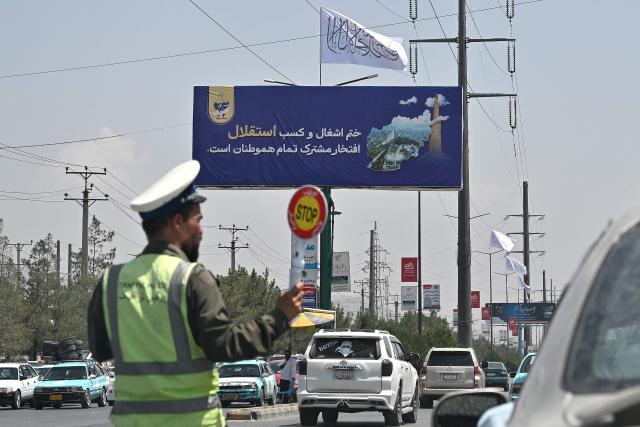 A newly setup billboard reading 'Ending the occupation and gaining Independence is the pride of all compatriots', is displayed along a busy road as a traffic policeman directs  vehicles in Kabul on August 13, 2026 ahead of the fifth anniversary marking the Taliban's return to power. (Photo by Wakil KOHSAR / AFP)