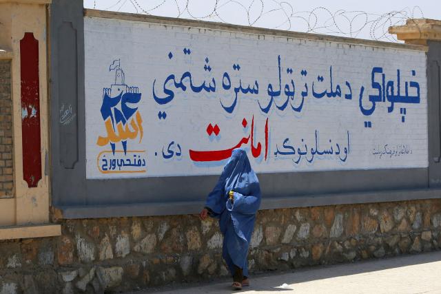 An Afghan burqa-clad woman walks past a mural commemorating the fifth anniversary marking the Taliban's return to power, in Afghanistan's Ghazni province on August 13, 2026. (Photo by Mohammad Faisal NAWEED / AFP)