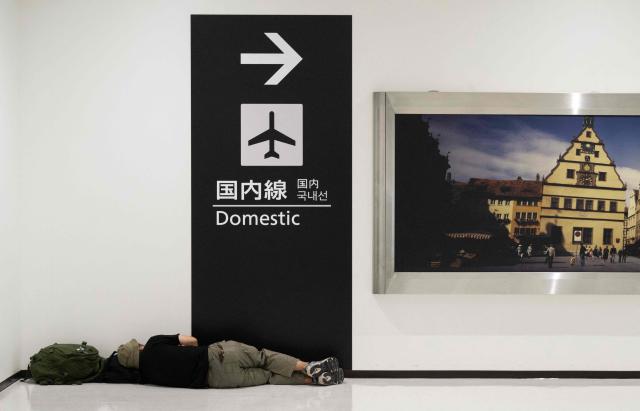 TOPSHOT - A passenger sleeps at the Narita International Airport in Narita, Chiba prefecture on August 14, 2026. At least four people died in eastern Japan after "unprecedented" heavy rain that left thousands stranded at Narita airport overnight and snarled up roads and rail services, authorities said. (Photo by ANDREW CABALLERO-REYNOLDS / AFP)