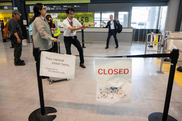 An airport employee explains to passengers that an entrance to the train station is closed  at the Narita International Airport in Narita, Chiba prefecture on August 14, 2026. At least four people died in eastern Japan after "unprecedented" heavy rain that left thousands stranded at Narita airport overnight and snarled up roads and rail services, authorities said. (Photo by ANDREW CABALLERO-REYNOLDS / AFP)