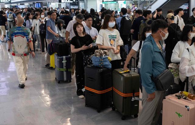 TOPSHOT - Passengers line up to enter the train station at the Narita International Airport in Narita, Chiba prefecture on August 14, 2026, after many of the train lines to the airport were closed. At least four people died in eastern Japan after "unprecedented" heavy rain that left thousands stranded at Narita airport overnight and snarled up roads and rail services, authorities said. (Photo by ANDREW CABALLERO-REYNOLDS / AFP)