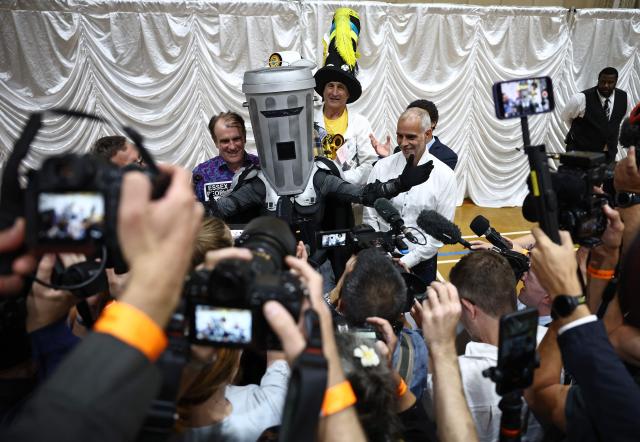 Candidates, including Count Binface (C), poses with other candidates following the declaration of the Clacton by-election at Clacton Leisure Centre, eastern England on August 14, 2026. Hard-right British politician Nigel Farage of the Reform UK party, was declared on August 14, the winner of an unusual by-election that pitted him against joke candidate Count Binface. (Photo by Henry NICHOLLS / AFP)