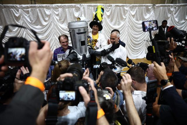 Candidates, including Count Binface (C), poses with other candidates following the declaration of the Clacton by-election at Clacton Leisure Centre, eastern England on August 14, 2026. Hard-right British politician Nigel Farage of the Reform UK party, was declared on August 14, the winner of an unusual by-election that pitted him against joke candidate Count Binface. (Photo by Henry NICHOLLS / AFP)
