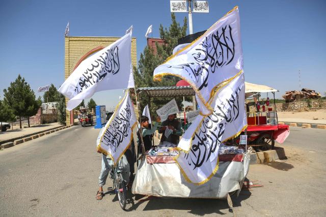 An Afghan boy buys a Taliban flag from a roadside vendor in Afghanistan's Ghazni province on August 14, 2026 ahead of the fifth anniversary of the Taliban government's return to power. (Photo by Mohammad Faisal NAWEED / AFP)
