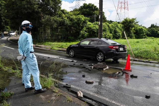 An utility worker looks on as a car drives around a manhole on a flood damaged road in Sakura, Chiba prefecture on August 14, 2026. At least four people died in eastern Japan after "unprecedented" heavy rain that left thousands stranded at Narita airport overnight and snarled up roads and rail services, authorities said. (Photo by ANDREW CABALLERO-REYNOLDS / AFP)