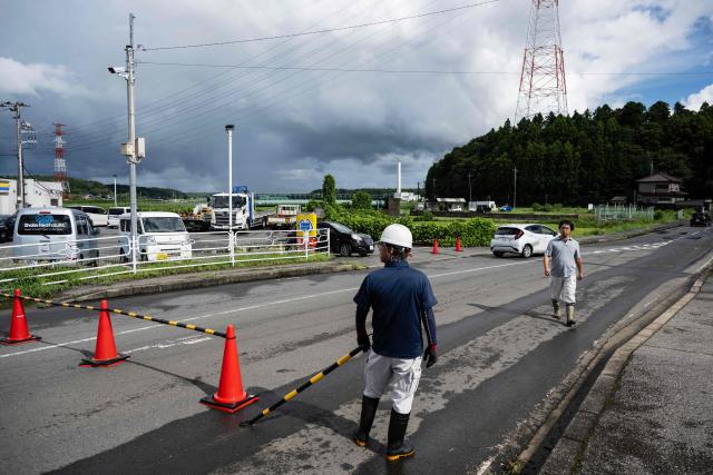 Utility workers block a road to flood damages further down in Sakura, Chiba prefecture on August 14, 2026. At least four people died in eastern Japan after "unprecedented" heavy rain that left thousands stranded at Narita airport overnight and snarled up roads and rail services, authorities said. (Photo by ANDREW CABALLERO-REYNOLDS / AFP)