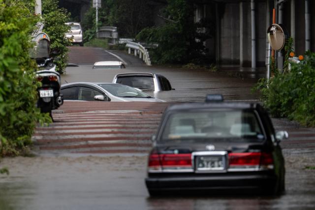 Abandoned cars are seen partially submerged on a flooded road in Sakura, Chiba prefecture on August 14, 2026. At least four people died in eastern Japan after "unprecedented" heavy rain that left thousands stranded at Narita airport overnight and snarled up roads and rail services, authorities said. (Photo by ANDREW CABALLERO-REYNOLDS / AFP)