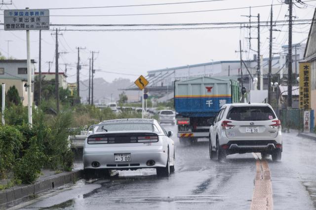 Vehicles drive around an abandoned car on a road in Sakura, Chiba prefecture on August 14, 2026. At least four people died in eastern Japan after "unprecedented" heavy rain that left thousands stranded at Narita airport overnight and snarled up roads and rail services, authorities said. (Photo by ANDREW CABALLERO-REYNOLDS / AFP)