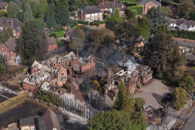 An aerial view shows smoke rising from a fire-damaged house, south of Stourbridge town centre in central England on August 14, 2026. Firefighters continued Friday to extinguish wildfires that began on August 13, tearing through several homes, with residents evacuated and "extensive" damage reported. (Photo by Darren Staples / AFP)