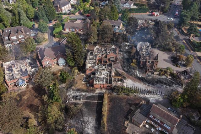 An aerial view shows smoke rising from fire-damaged houses, south of Stourbridge town centre in central England on August 14, 2026. Firefighters continued Friday to extinguish wildfires that began on August 13, tearing through several homes, with residents evacuated and "extensive" damage reported. (Photo by Darren Staples / AFP)
