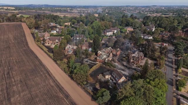 An aerial view shows smoke rising from a group of fire-damaged houses, beside burnt fields, south of Stourbridge town centre in central England on August 14, 2026. Firefighters continued Friday to extinguish wildfires that began on August 13, tearing through several homes, with residents evacuated and "extensive" damage reported. (Photo by Darren Staples / AFP)