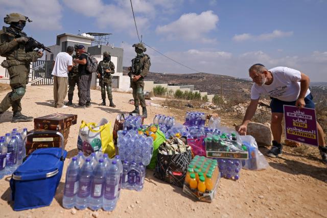 Israeli soldiers stand in front of the entrance of a besieged Palestinian house by Israeli settlers in the village of Qusra, south of Nablus, in the occupied West Bank, on August 14, 2026, after Israeli leftist activists and solidarity volunteers placed supplies to be taken inside the house. Israeli forces on August 13 moved against rogue settlers laying siege to Palestinians amid unusually strong US criticism, even as Israel inaugurated an emblematic settlement elsewhere in the West Bank. Settlers at Qusra near Nablus since August 9 have blockaded Palestinian homes, including one owned by a US citizen, with residents saying they have been cut off from food and other supplies. (Photo by JAAFAR ASHTIYEH / AFP)