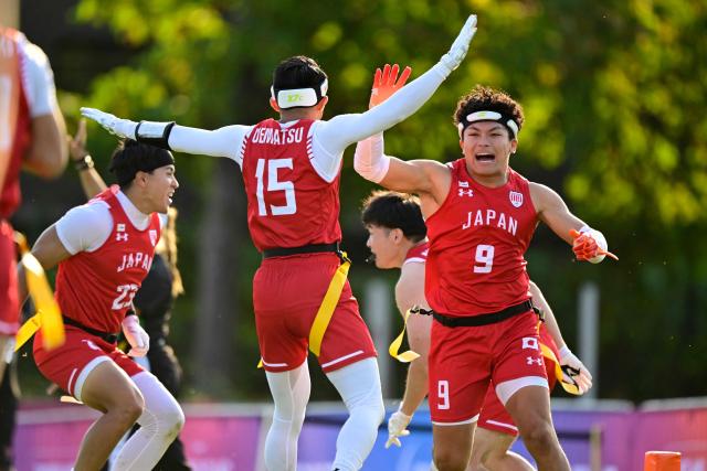 Japan's Haruki Suzuki (R) celebrates with Japan's Ryohei Uematsu (C, No 15) during the men's match between Japan and Canada at the "IFAF World Flag" World Championship in flag football in Duesseldorf, western Germany, on August 14, 2026. (Photo by Ina FASSBENDER / AFP)