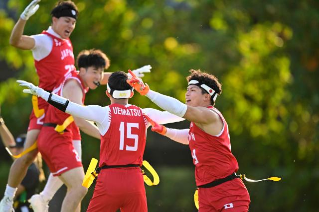 Japan's Haruki Suzuki (R) celebrates with Japan's Ryohei Uematsu (C, No 15) during the men's match between Japan and Canada at the "IFAF World Flag" World Championship in flag football in Duesseldorf, western Germany, on August 14, 2026. (Photo by Ina FASSBENDER / AFP)